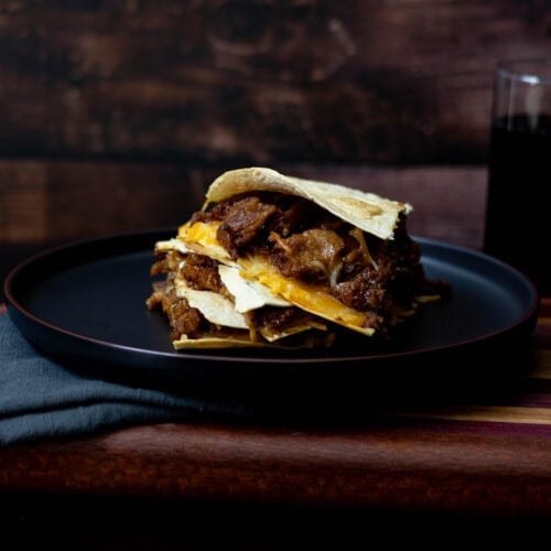 Shredded BBQ Seitan Quesadilla with melted cheese plated on a black plate, sitting on a wooden cutting board.