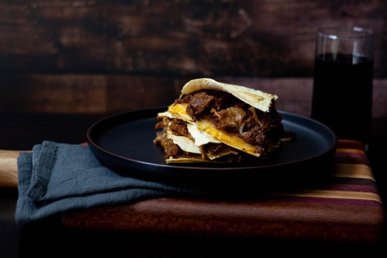 Shredded BBQ Seitan Quesadilla with melted cheese plated on a black plate, sitting on a wooden cutting board.