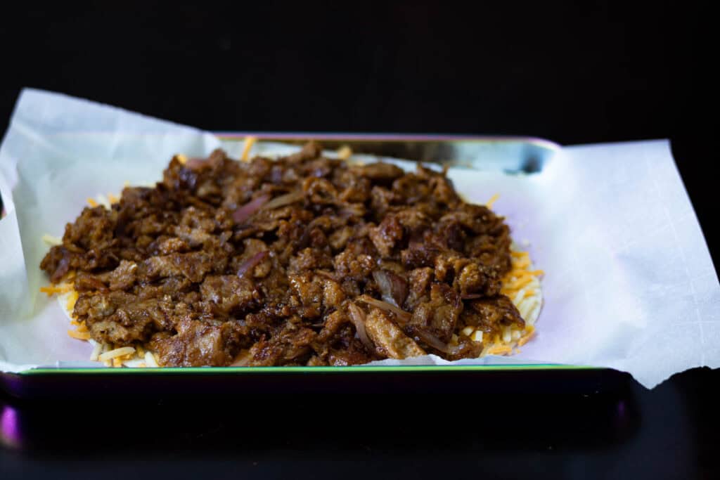 Tortilla with vegan cheese and shredded BBQ seitan, sitting on a parchment paper-lined cookie sheet.