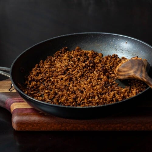 High Protein Vegan Bacon Bits in a skillet, sitting on a wooden cutting board with a wooden spoon.