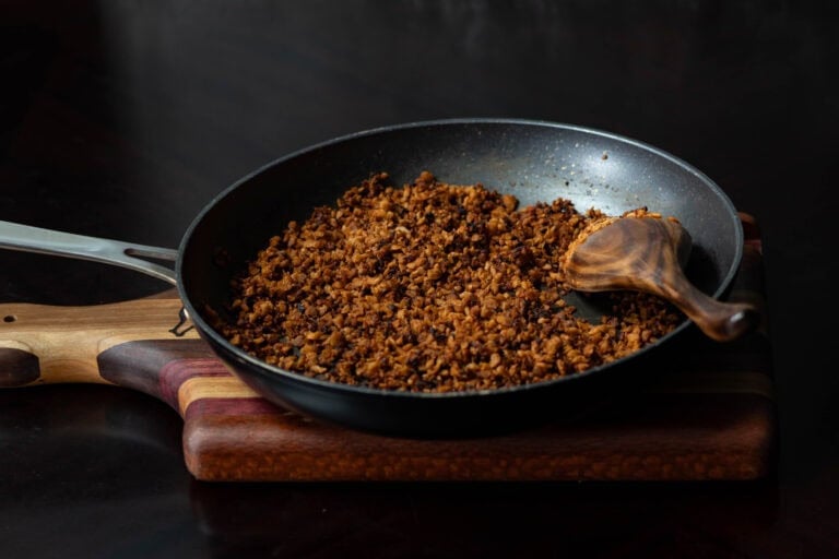 High Protein Vegan Bacon Bits in a skillet, sitting on a wooden cutting board with a wooden spoon.