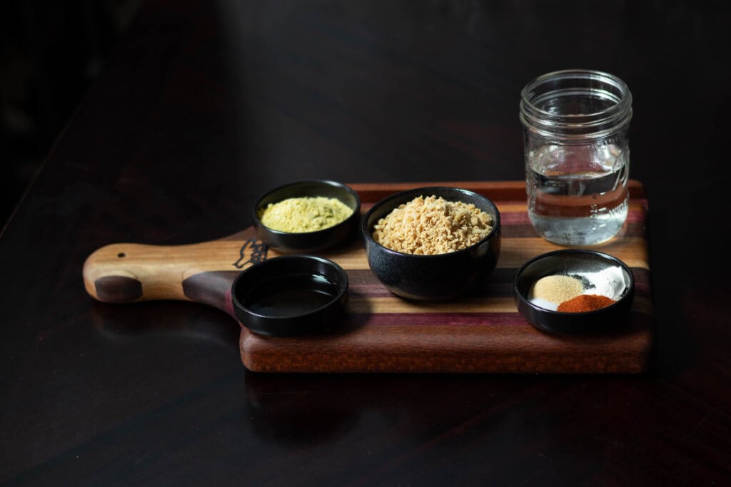 Ingredients for recipe sitting on a wooden cutting board - soy sauce, maple syrup, nutritional yeast, TVP, water, and spices.