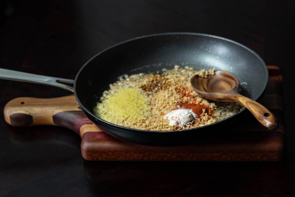 All ingredients for recipe in a skillet, uncooked, sitting on a wooden cutting board.
