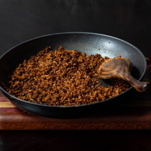 High Protein Vegan Bacon Bits in a skillet, sitting on a wooden cutting board.