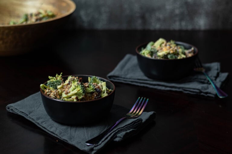 Two medium bowls with high protein vegan broccoli salad, sitting on blue-grey napkins with forks.