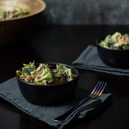 Two medium bowls with high protein vegan broccoli salad, sitting on blue-grey napkins with forks.