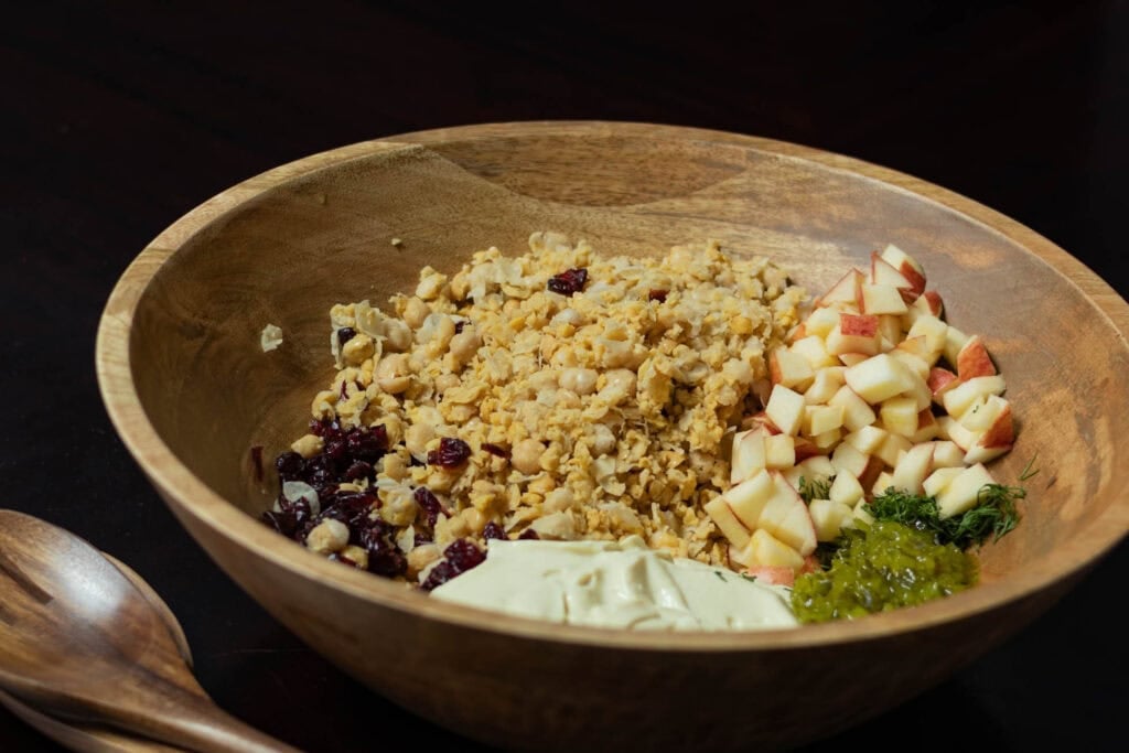 All of the ingredients for the no mayo chickpea salad in a large wooden bowl, unmixed.