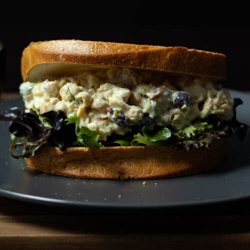 Chickpea Salad Sandwich with fresh mixed greens sitting on a grey plate, placed on a wooden cutting board.