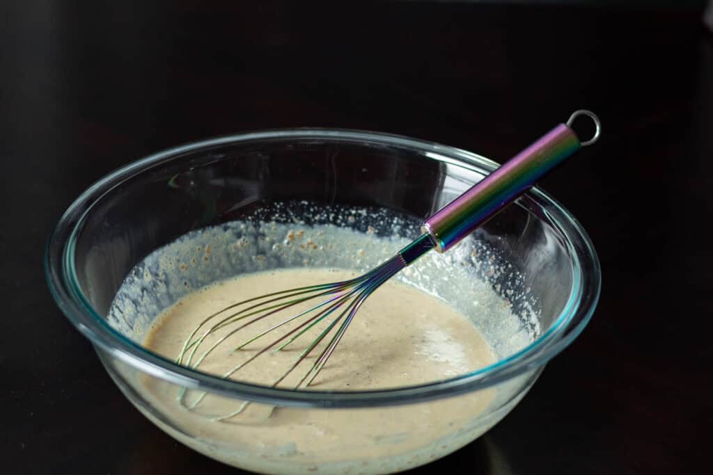 Mixed wet ingredients in a large glass bowl sitting on a dark table.