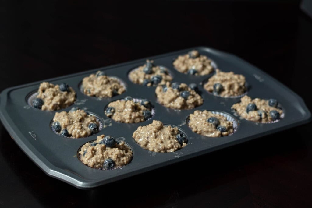 Blueberry Muffin batter divided even across a silver muffin tray.