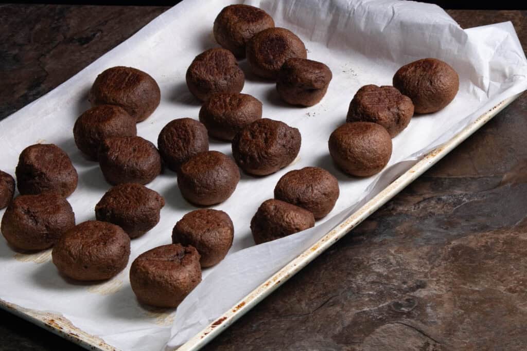 Cooked chocolate seitan balls on a parchment paper-lined cookie sheet sitting on a table.