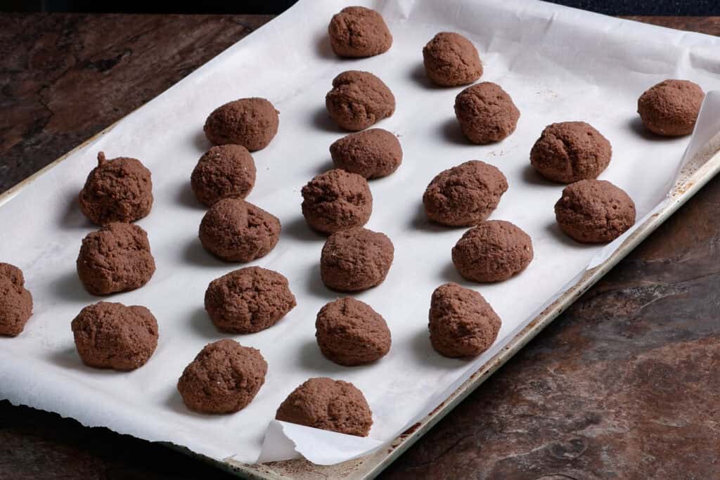 Small balls of chocolate seitan dough sitting on a parchment paper-lined baking sheet.
