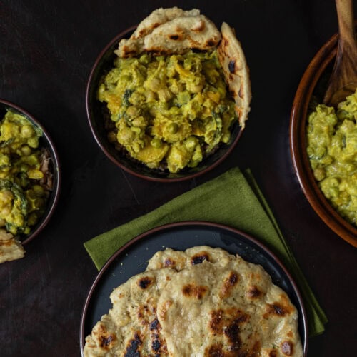 Two bowls of Butternut Squash Chickpea Curry and naan, a serving bowl of curry and a plate of naan.