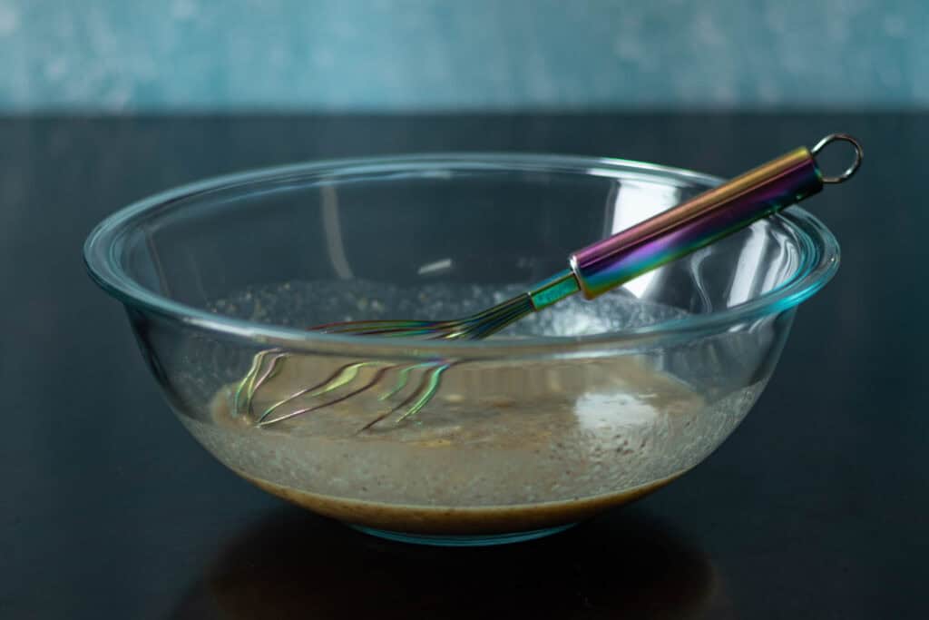 Large glass bowl with all of the wet ingredients mixed and a rainbow whisk.
