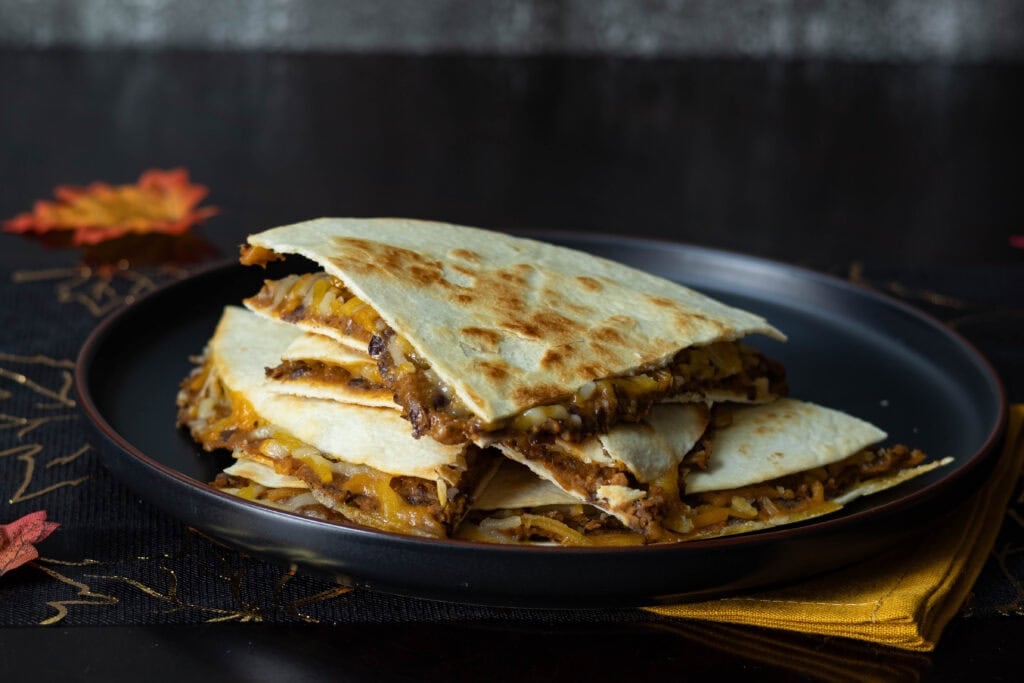 Pumpkin and Black Bean Quesadillas sitting on a black plate on a fall-decorated table.