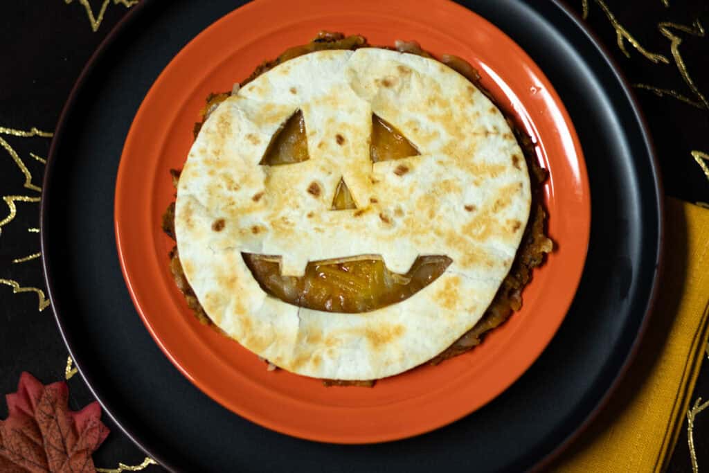 Black bean and pumpkin quesadilla with a little jack-o-lantern face cut out of the top tortilla. Styled with a halloween vibe.