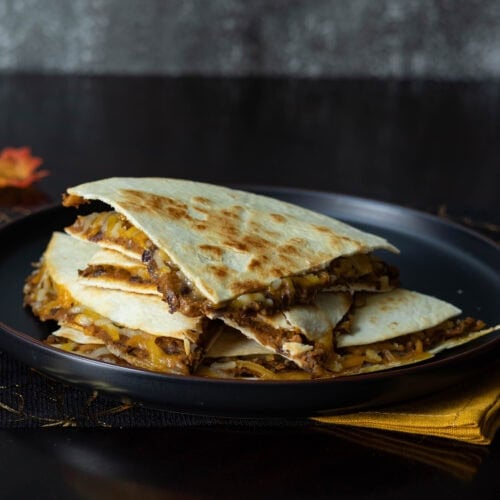 Pumpkin and Black Bean Quesadillas sitting on a black plate on a fall-decorated table.