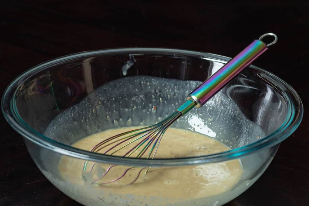 Wet ingredients for chocolate orange muffins mixed together in large glass bowl with rainbow whisk.