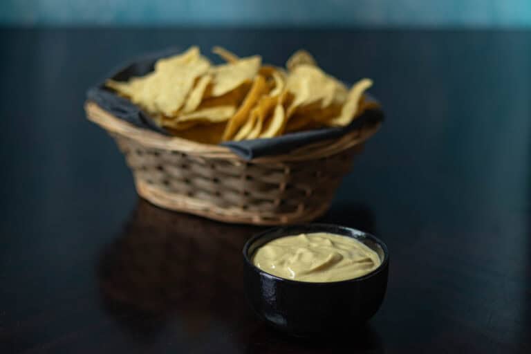 Bowl of high protein vegan cheese sauce with a basket of tortilla chips in the background.