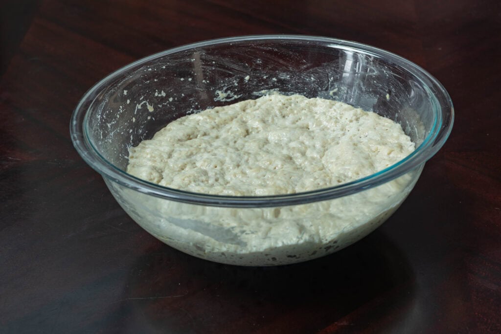 Bread dough that has doubled in size in a large glass bowl.