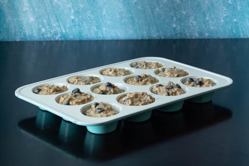 Muffin tin filled with blueberry lemon muffin batter.