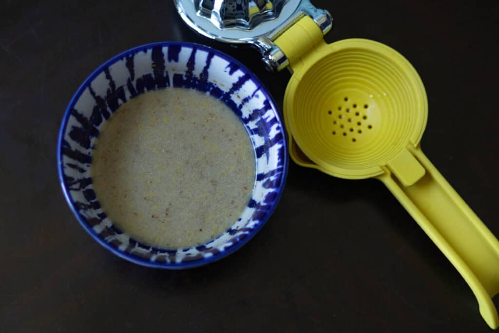Small blue and white bowl with lemon flax egg, with a lemon squeezer to the side.