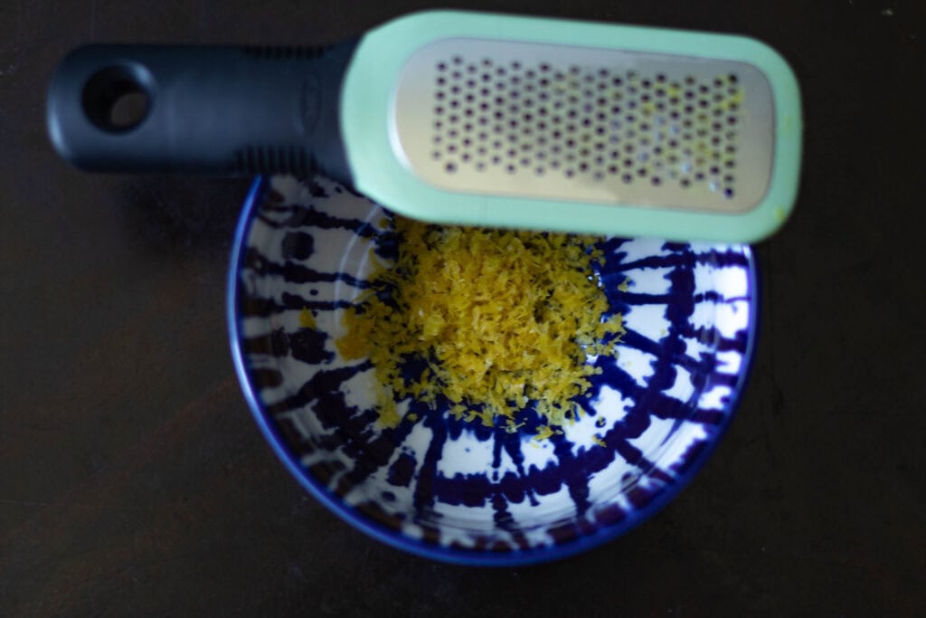 Small blue and white bowl full with lemon zest. Lemon zester sitting to the side.