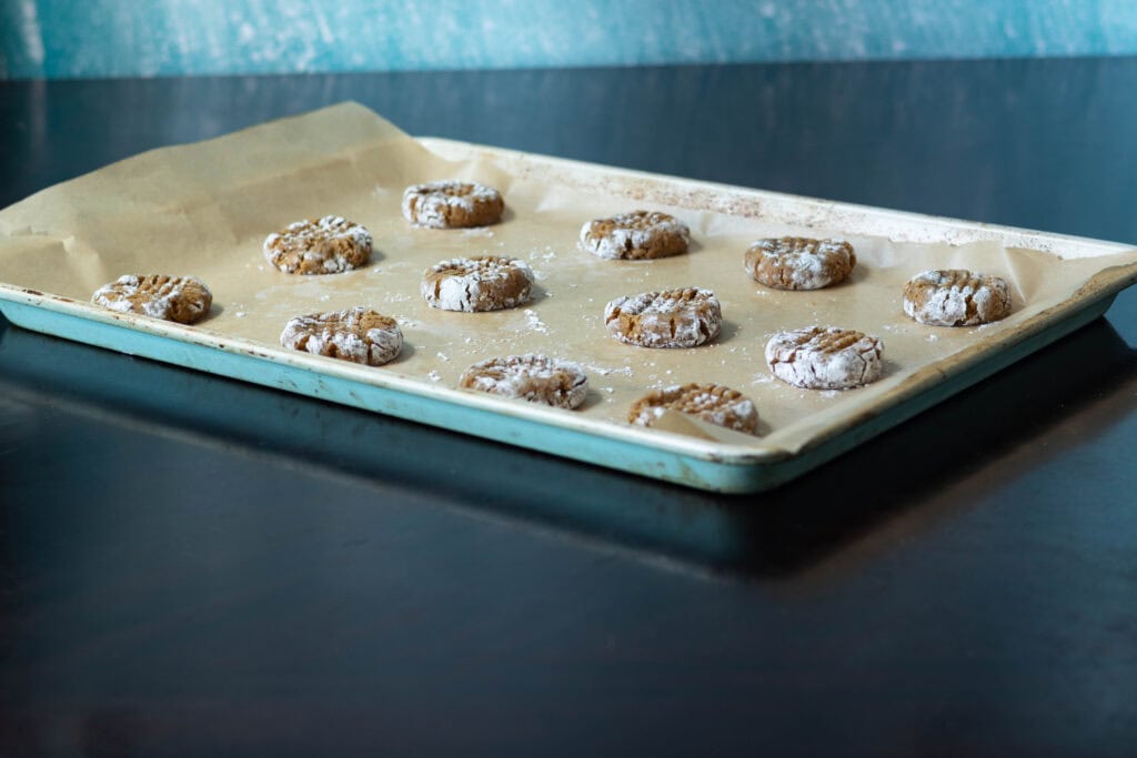 Peanut butter cookie dough rolled out into little balls with classic fork marks on a parchment paper-lined baking sheet. Cookies are not baked yet.