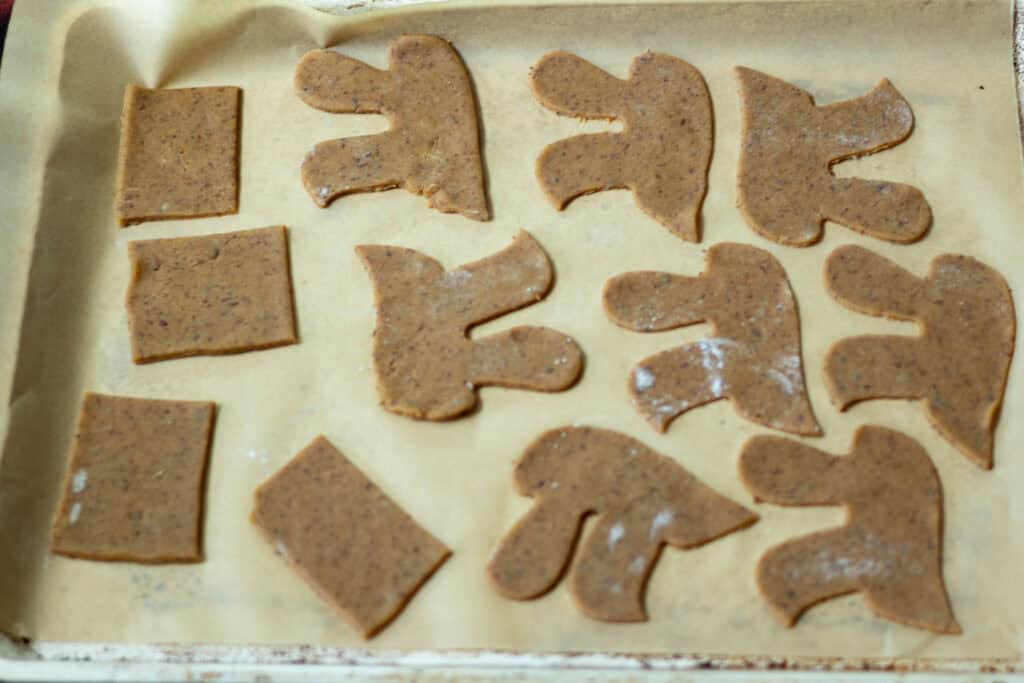 Baking sheet lined with parchment paper, peanut butter cookie dough in different shapes laying on top, uncooked.