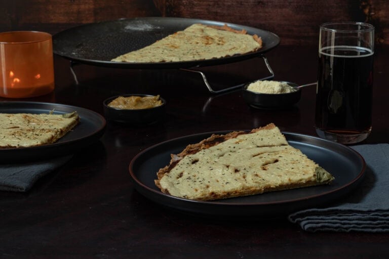 Two plates of large pizza slices, with the remaining pizza in a pan in the background.