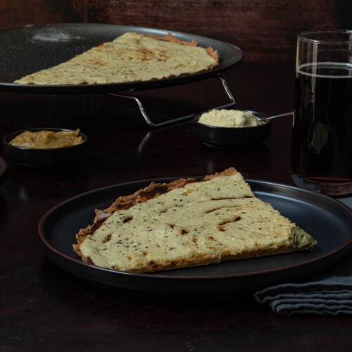 Two plates of large pizza slices, with the remaining pizza in a pan in the background.
