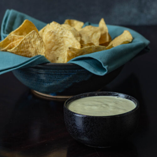Large bowl of tortilla chips sitting next to a smaller bowl of homemade vegan queso.
