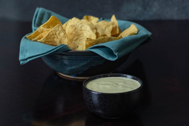 Large bowl of tortilla chips sitting next to a smaller bowl of homemade vegan queso.