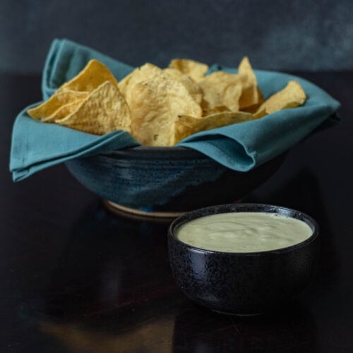 Large bowl of tortilla chips sitting next to a smaller bowl of homemade vegan queso.