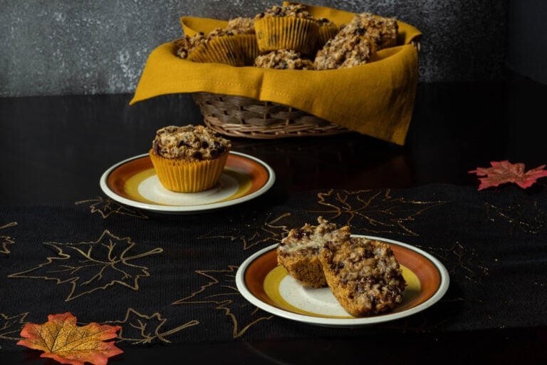 Pumpkin Craisin Muffins on small plates with a basket of muffins in the background. The table is decorated with a Fall theme.
