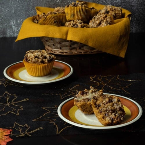 Pumpkin Craisin Muffins on small plates with a basket of muffins in the background. The table is decorated with a Fall theme.