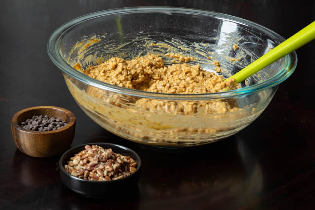 Large bowl with muffin batter, sitting next to two small bowls with pecans and chocolate chips.