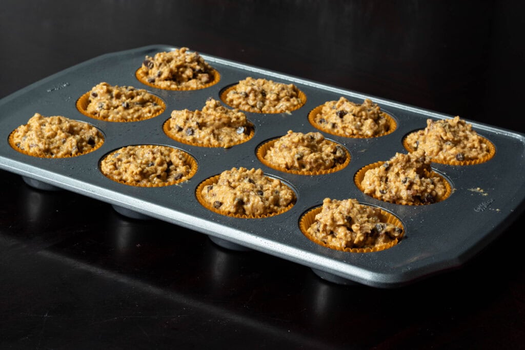 Metal muffin tray with uncooked muffin batter.