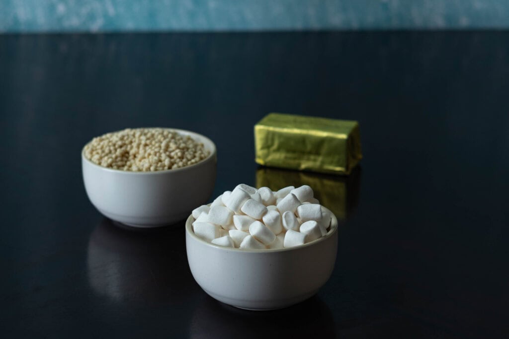 Ingredients for high protein rice crispy treats sitting on a table - mini marshmallows, edamame puffs, and vegan butter.