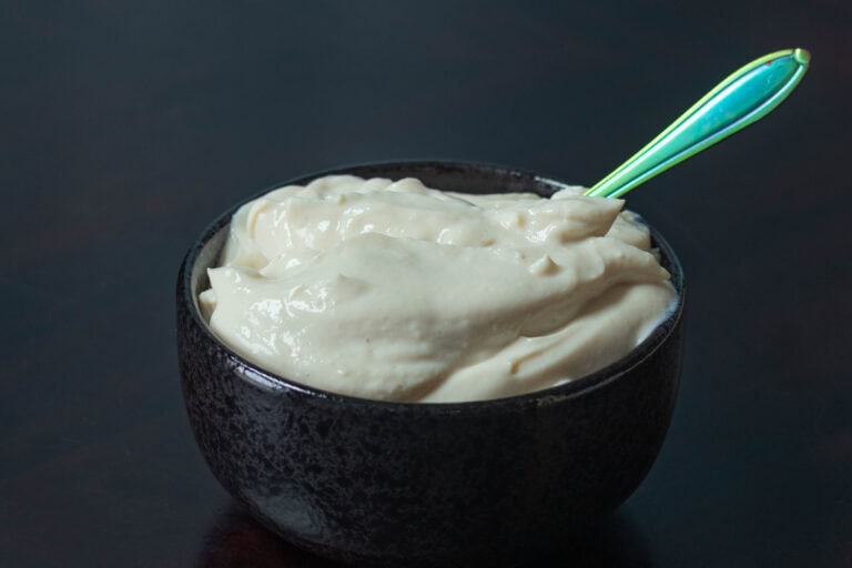 Small black bowl with high protein vegan sour cream and a small spoon.