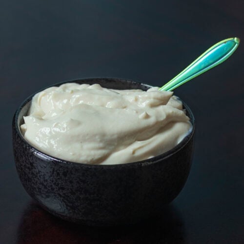 Small black bowl with high protein vegan sour cream and a small spoon.