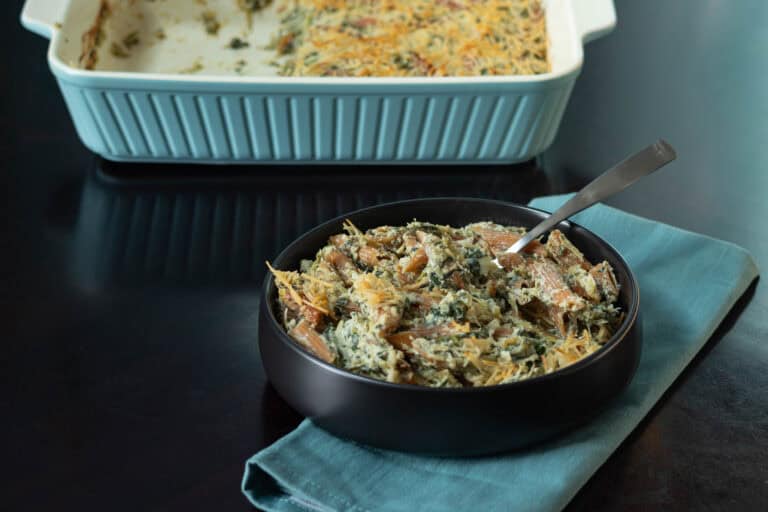 Spinach and artichoke pasta in a large bowl with a casserole dish with the leftover pasta in the background.