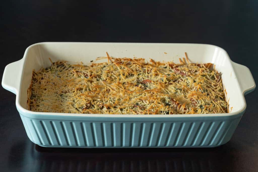Large casserole dish with spinach and artichoke pasta covered in toasted and browned vegan parmesan.