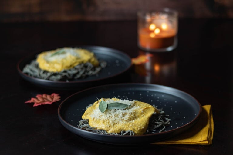 Two plates with black noodles topped with creamy pumpkin sauce and fresh sage. Styled with a Fall vibe.