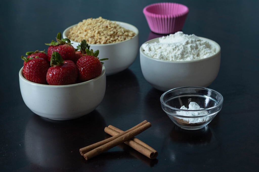 Dry ingredients for the strawberry muffins sitting on a table - strawberries, TVP, flour, and baking soda, baking powder, salt and cinnamon.