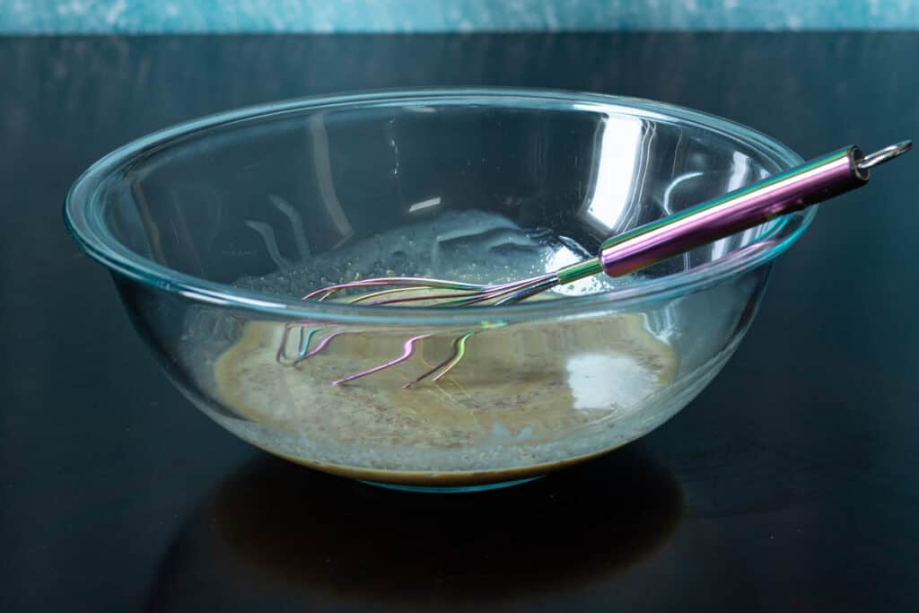 Wet ingredients mixed together in a glass bowl with a whisk.