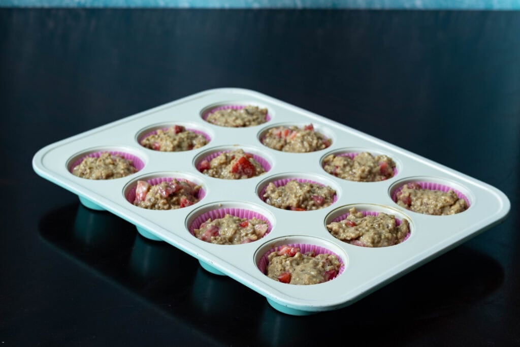 Muffin tray with uncooked strawberry muffin batter.