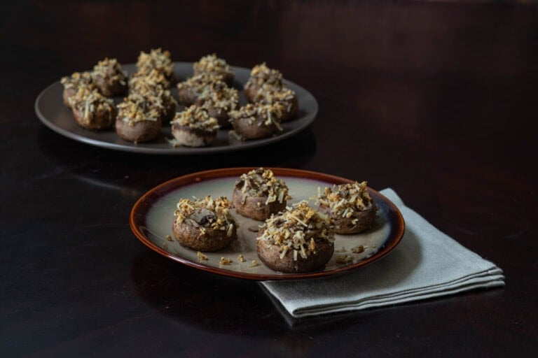 One small plate of stuffed mushrooms with a large serving plate of stuffed mushrooms behind.