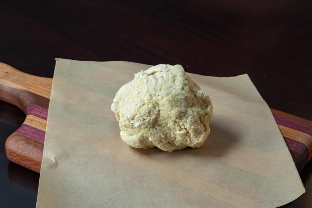 Pizza dough in a ball sitting on parchment paper.