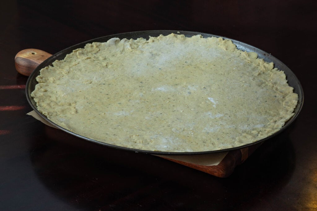 Uncooked pizza dough on a large pizza pan.